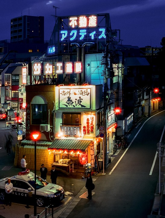 A police car is parked on a street corner in front of a building with neon signs at night.