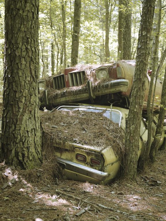 Two abandoned cars are stacked on top of each other in a forest.