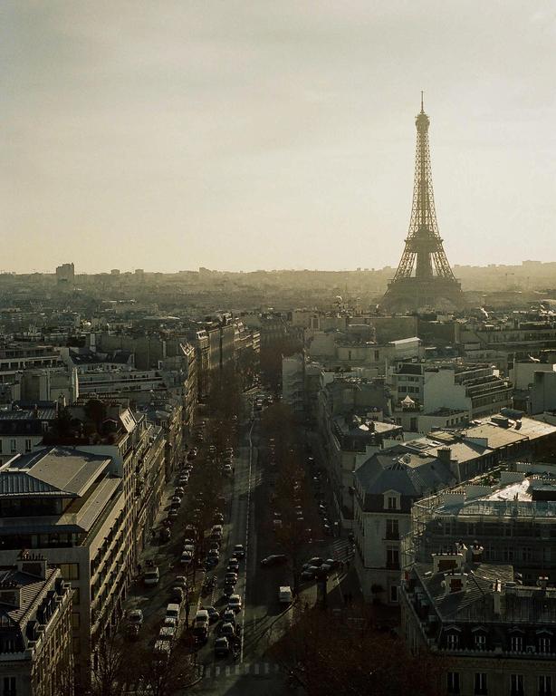 The Eiffel Tower rises above a city street filled with cars and buildings.