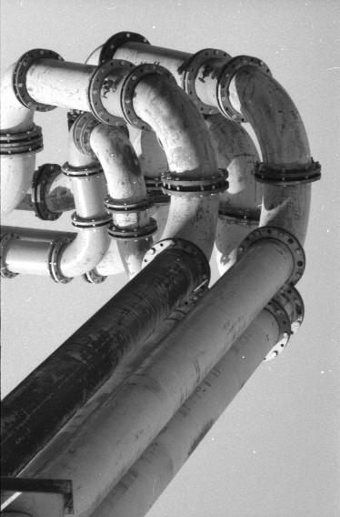 A complex arrangement of industrial pipes with flanges is shown against a plain background.