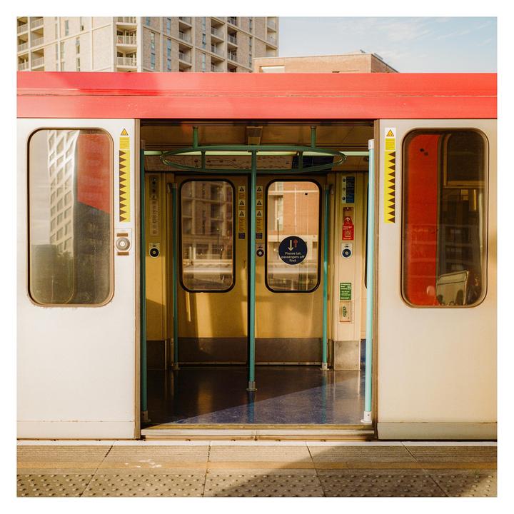 An open train door is visible from the platform with buildings in the background.