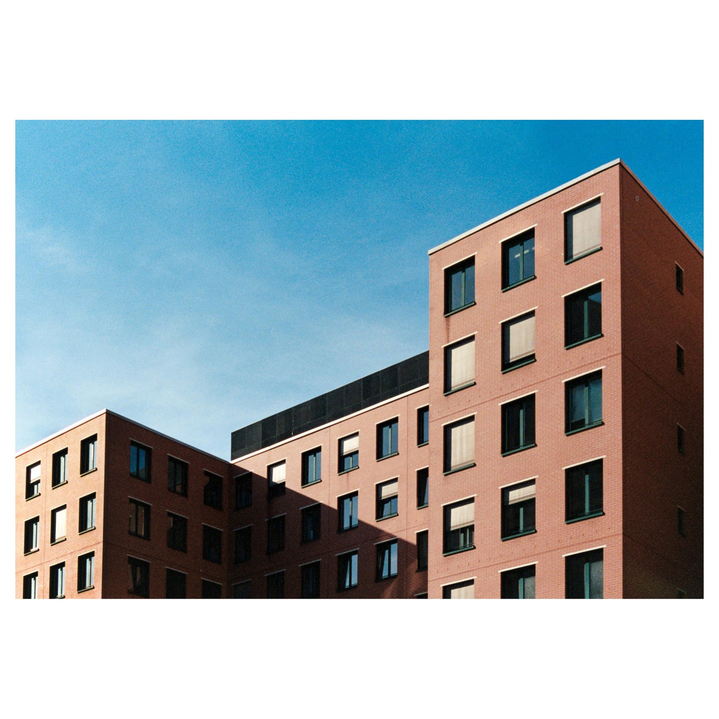 Two brick buildings with many windows are shown against a clear blue sky.