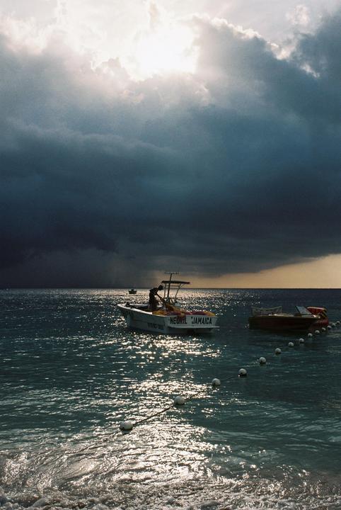 A boat with "Negril Jamaica" written on its stern is on the water under a dramatic, cloudy sky.