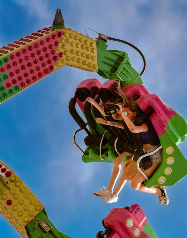 Two women are riding a colorful amusement park ride against a bright blue sky.