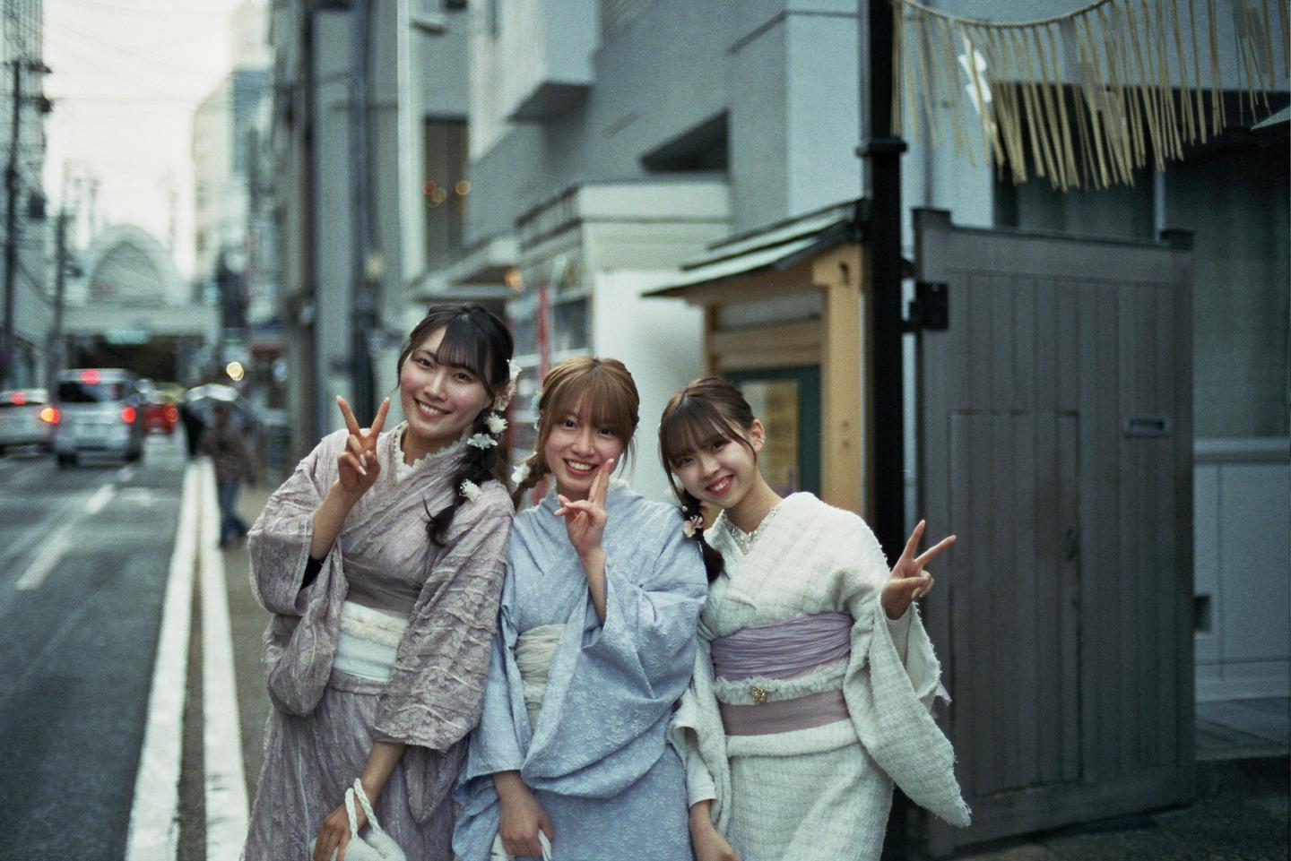 Three women in kimonos pose for a photo on a city street.
