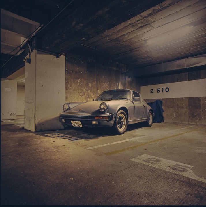 A dusty gray Porsche is parked in a concrete parking garage.