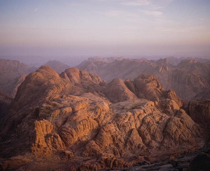 A vast mountain range with rugged, rocky peaks stretches into the distance under a soft, hazy sky.