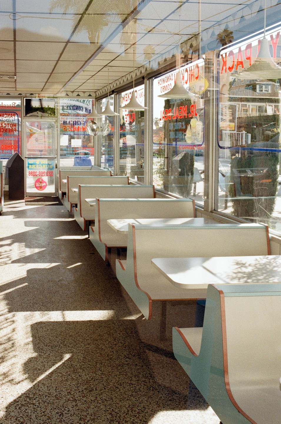 The interior of a diner with booths and tables is illuminated by sunlight streaming through large windows, casting shadows on the floor.