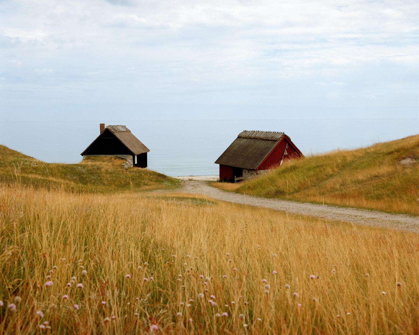 Two small sheds with thatched roofs sit on grassy hills overlooking the sea.