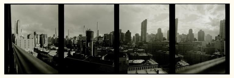 A panoramic view of a city skyline with numerous buildings and a water tower is seen from a terrace.