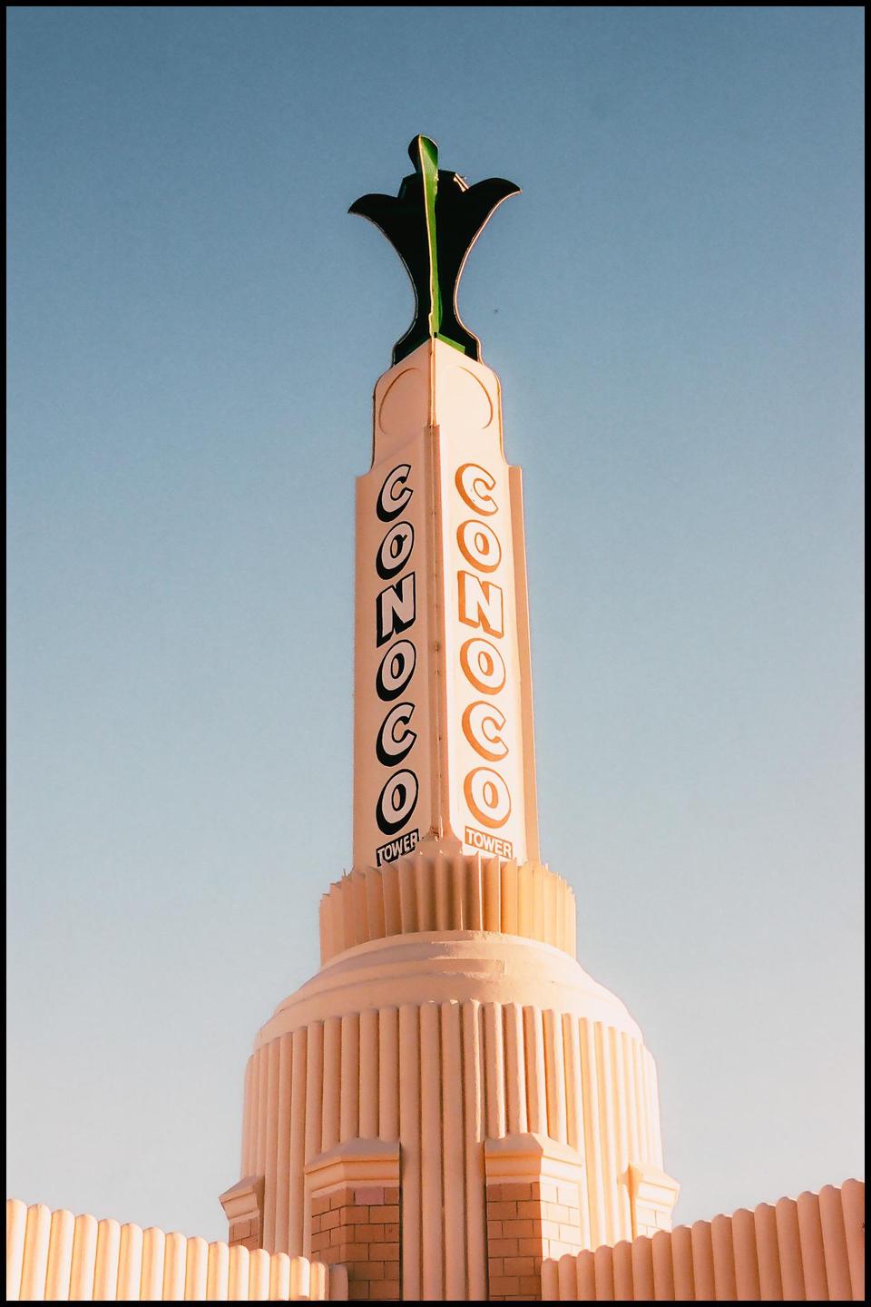 A tall, cream-colored tower with "CONOCO" written vertically on two sides stands against a clear blue sky.