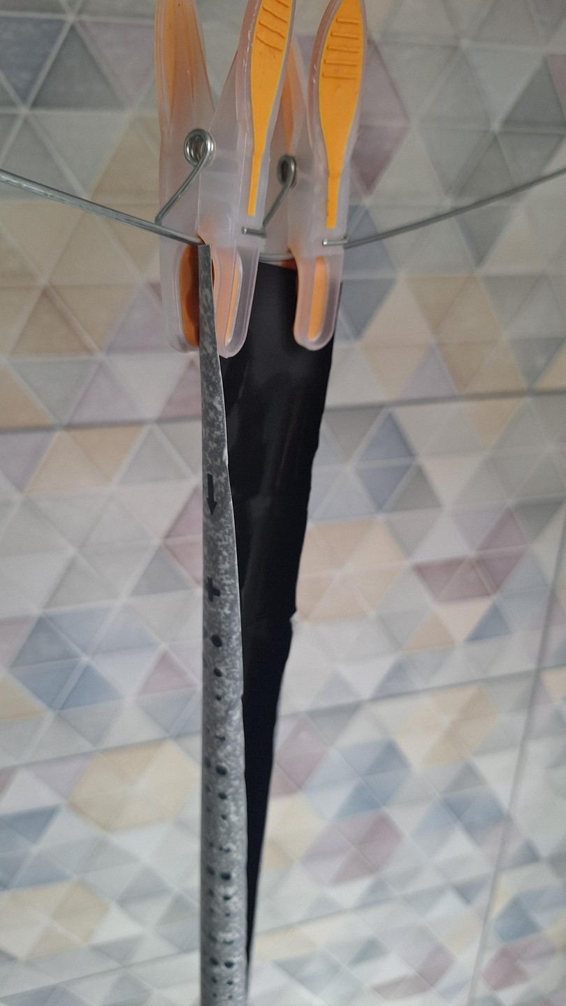 Two clothespins hold a strip of black film and a paper backing against a tiled wall.