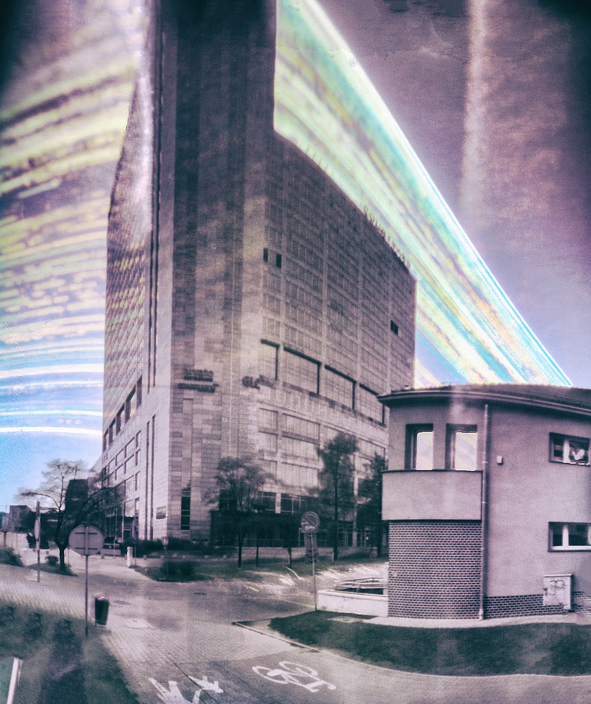 A tall building stands next to a smaller building with a curved wall, with a bright, colorful light streak across the sky.