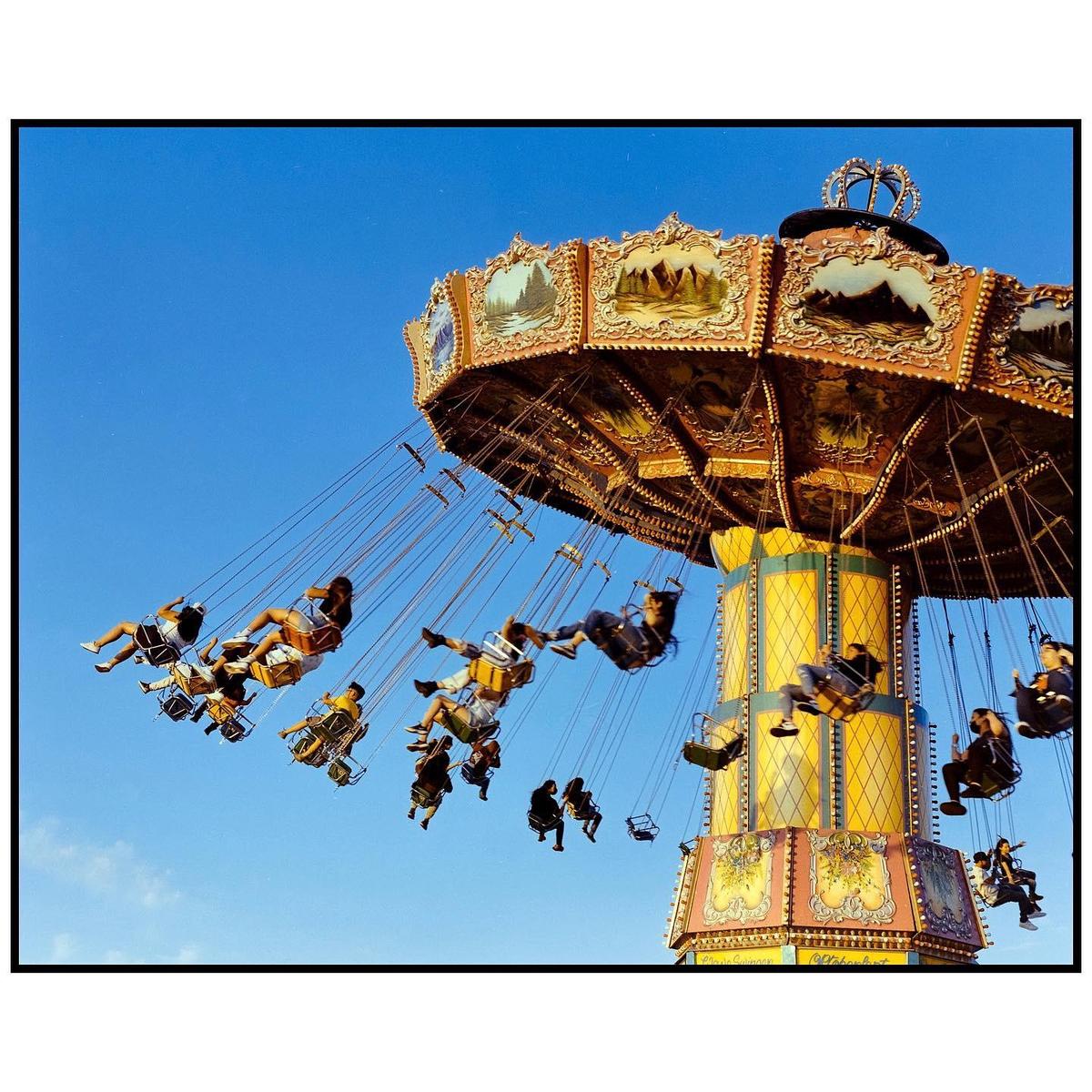 People ride a swing ride at an amusement park against a clear blue sky.