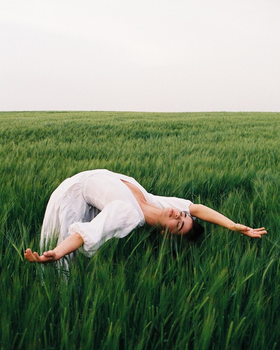 A woman in a white dress is bending backward in a field of green grass.