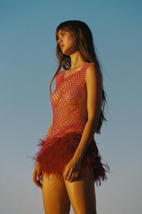 A woman in a red dress with a feathered skirt stands against a clear blue sky.