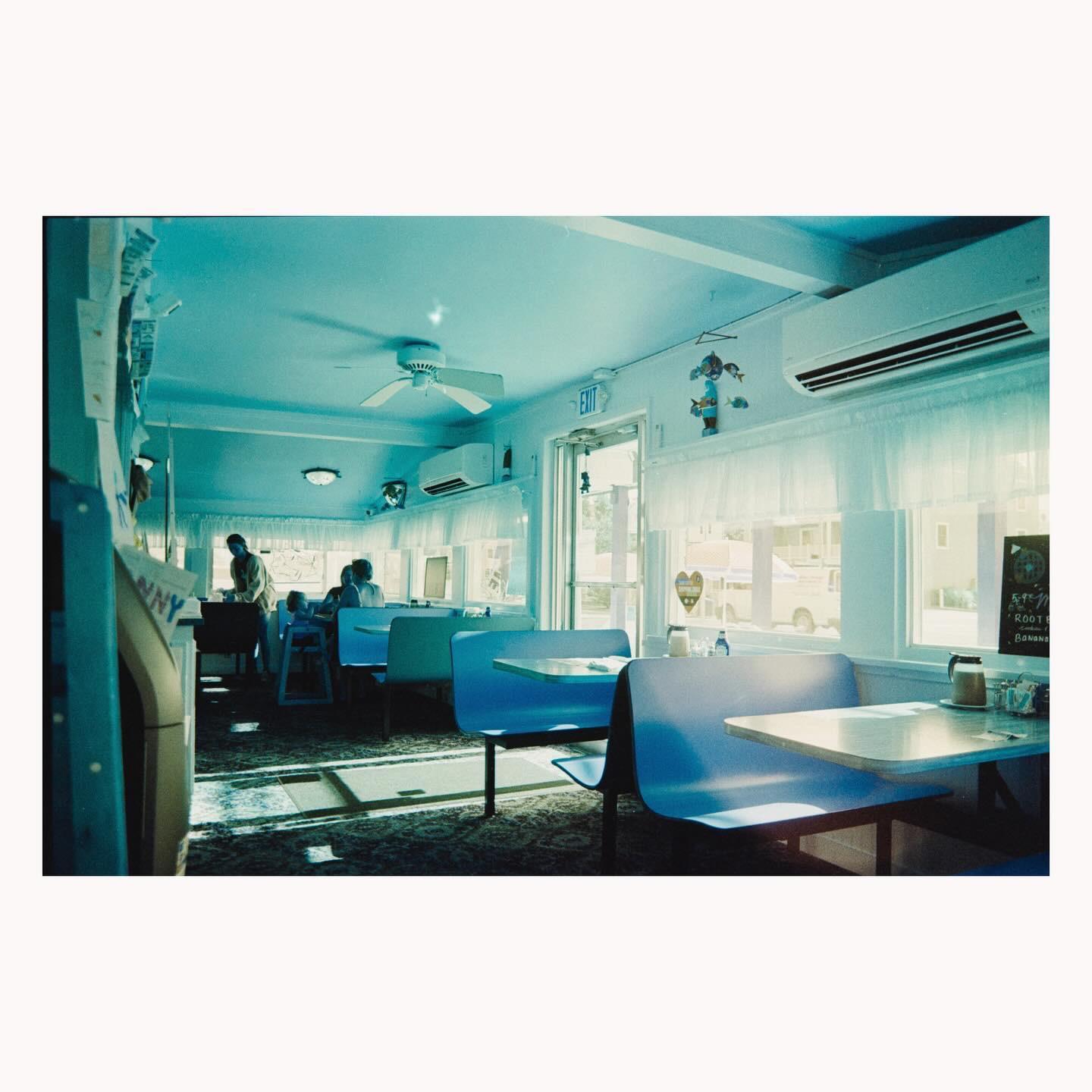 Sunlight streams into a diner with blue booths and a man standing near a counter.