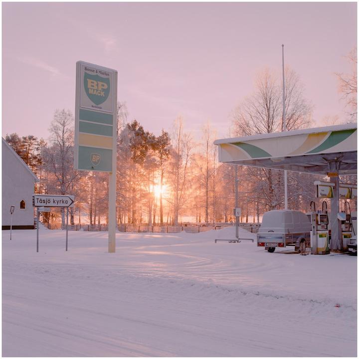 A gas station and a building are covered in snow with a bright sunset in the background.