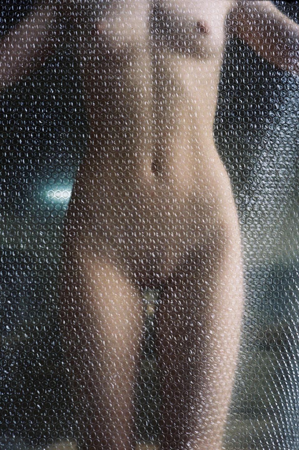 A nude woman is visible through a sheet of bubble wrap.