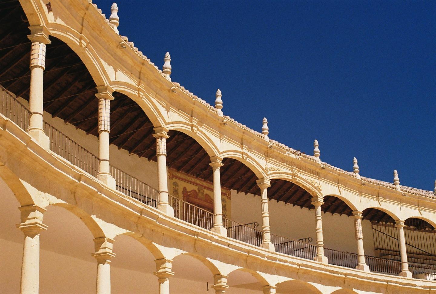A curved building with multiple arched balconies and columns is shown against a clear blue sky.