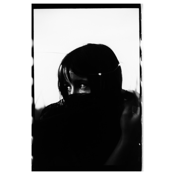 A woman with dark hair and bangs looks over a dark veil with string lights in her hair.