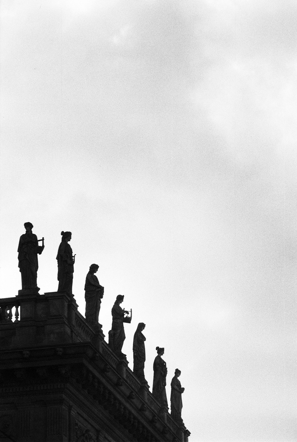 A row of statues stands silhouetted against a bright sky.