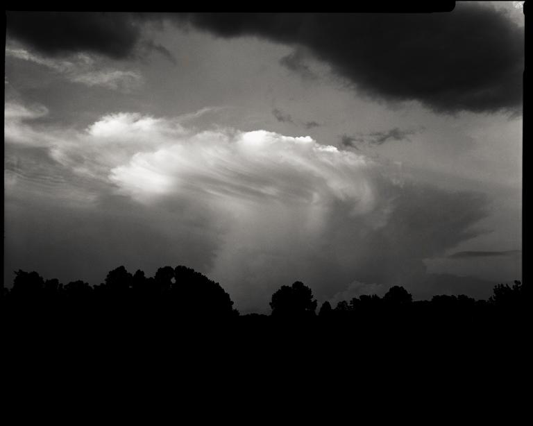 A dramatic sky with swirling clouds looms over a dark silhouette of trees.