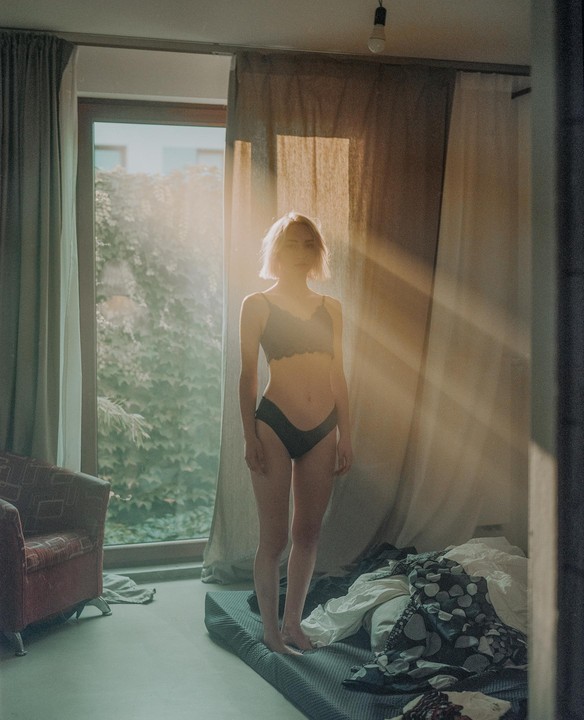 A woman stands in a sunlit room with light rays streaming through a window.