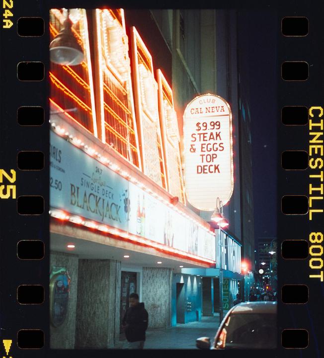 A man walks past a casino with neon signs at night.