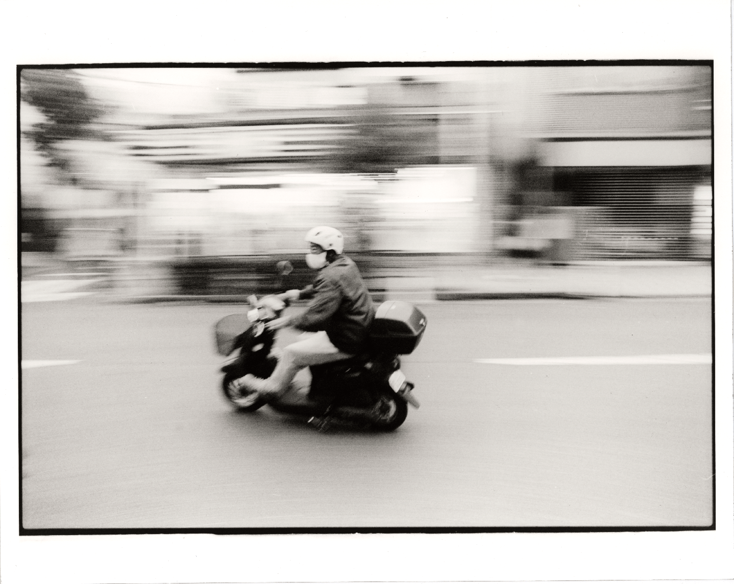 A person on a scooter drives past with a blurred background.