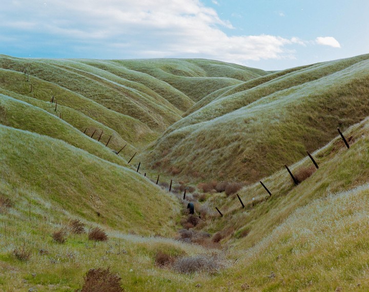 Rolling green hills with a fence line running through a valley under a cloudy sky.