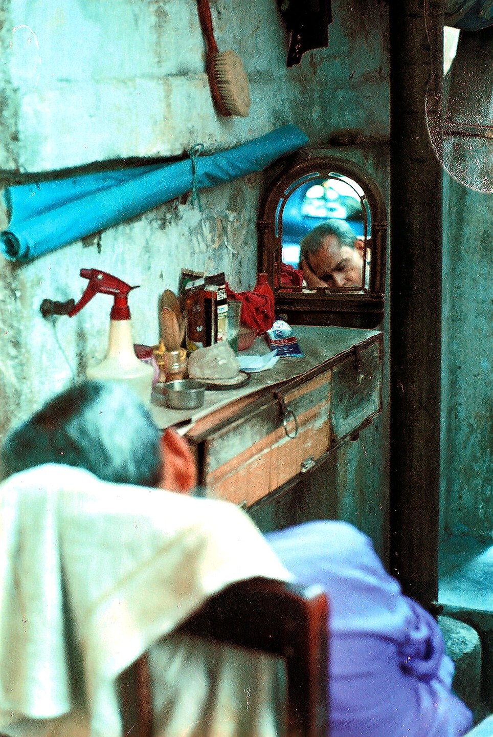 A man rests his head on a counter, reflected in a small mirror in a barbershop in Kolkata.