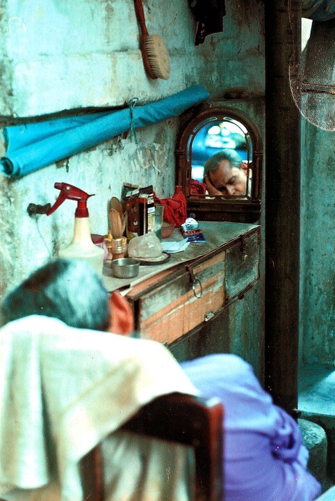 A man rests his head on a counter, reflected in a small mirror in a barbershop in Kolkata.