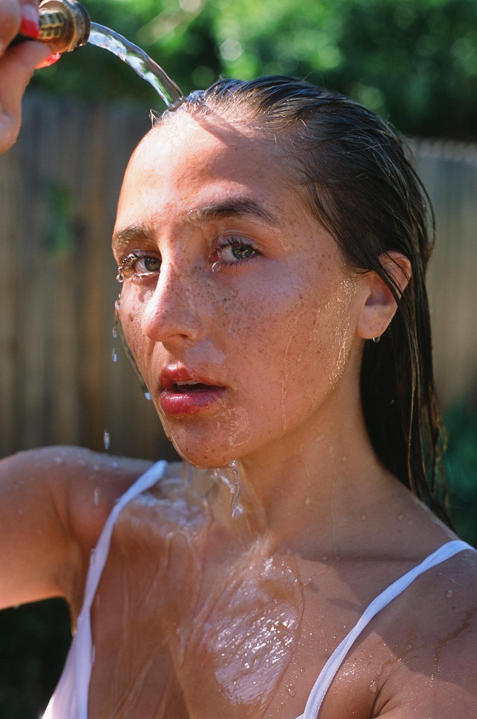 A woman with freckles is being rinsed with water from a hose.