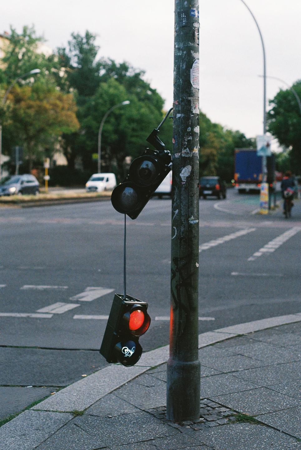 A broken traffic light hangs from a pole on a city street.