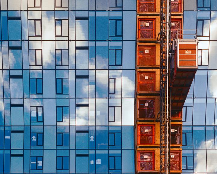 A construction elevator is attached to the side of a modern building with reflective windows.
