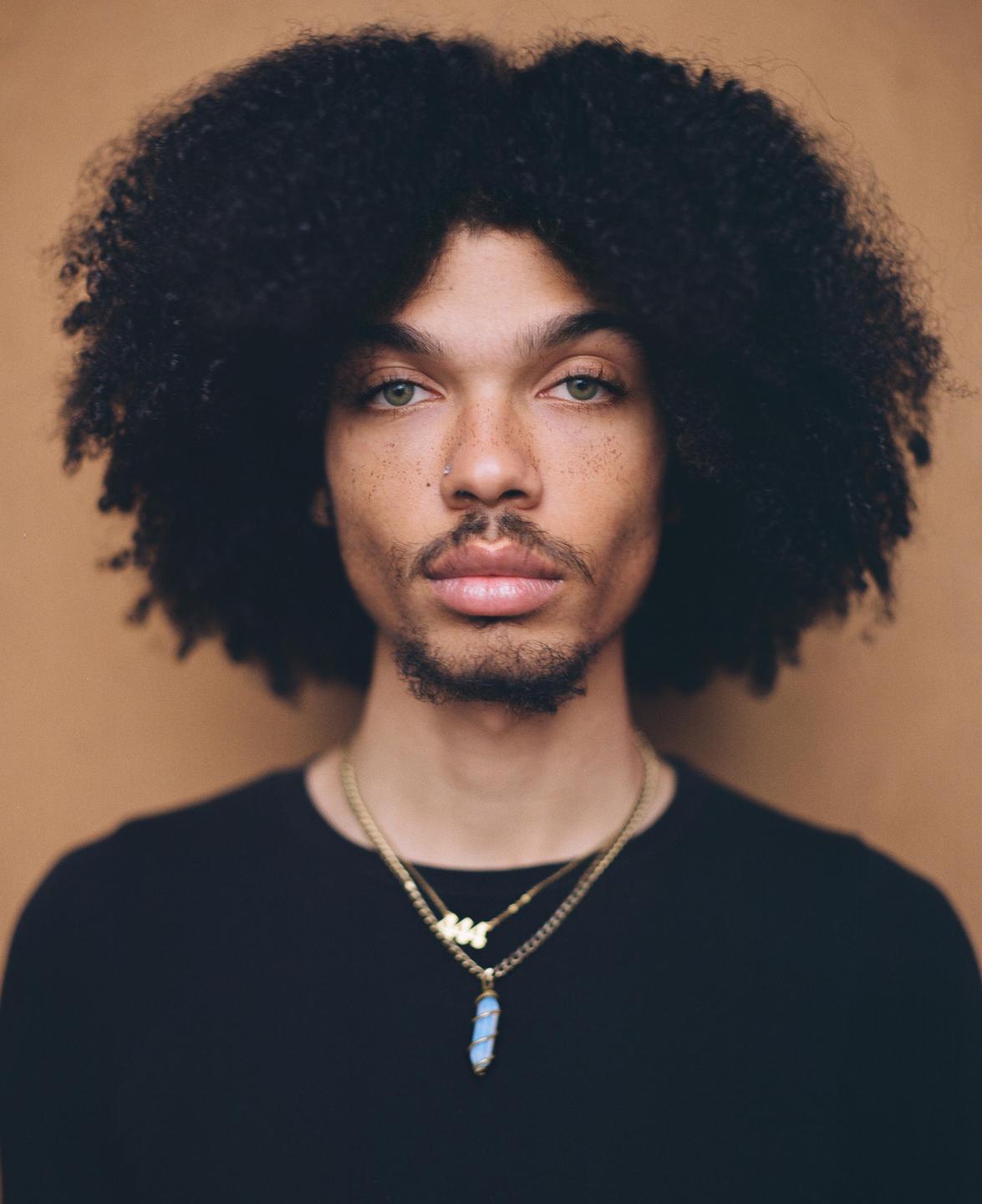 A man with an afro and a beard looks directly at the viewer.