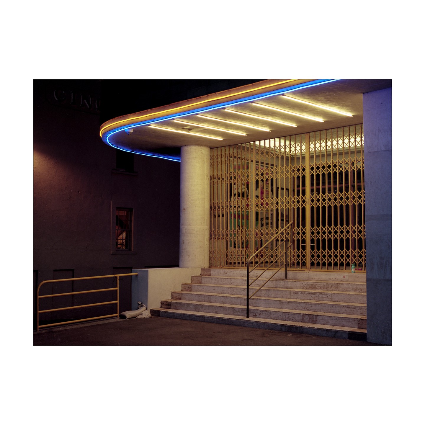 A building with neon lights and a closed gate stands at night.