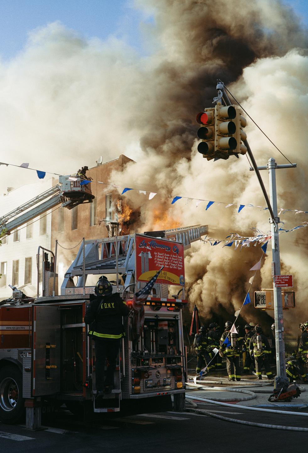 Firefighters work to extinguish a building fire that is producing a large amount of smoke on a city street.