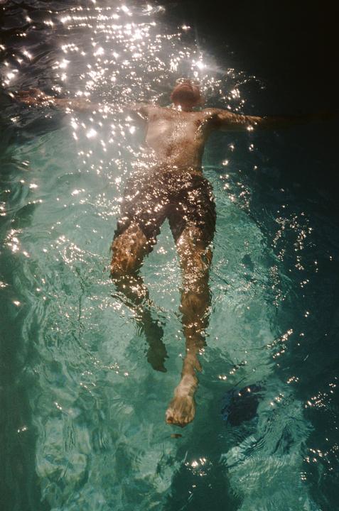 A man floats on his back in a body of water with sparkling light reflecting on the surface.
