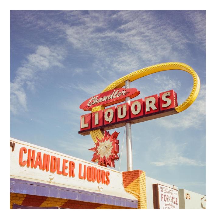 A red and yellow Chandler Liquors sign stands against a blue sky with wispy clouds.