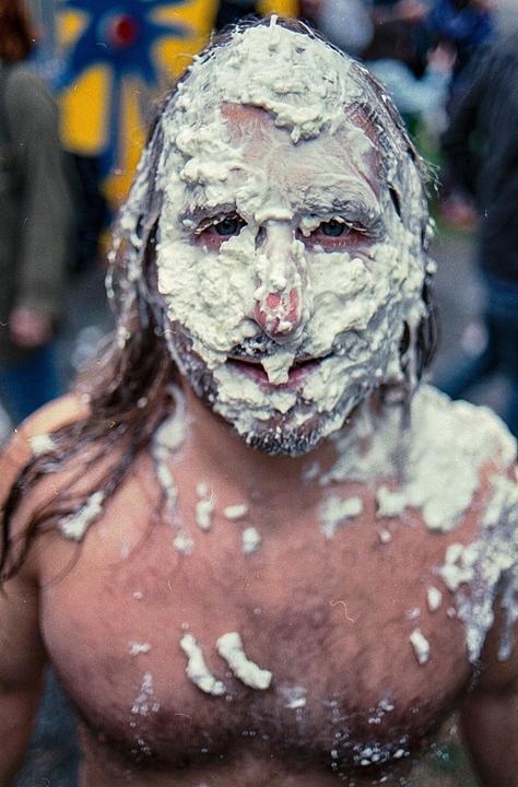 A man with long hair and a beard is covered in white cream on his face and chest.