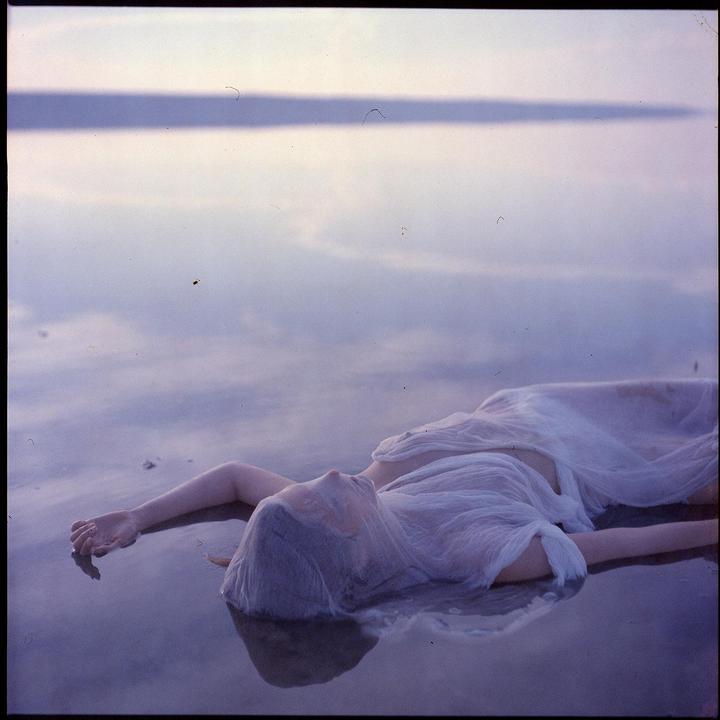 A woman in a white dress lies in shallow water with her face partially obscured by fabric.