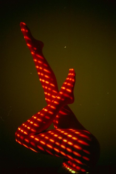 A person's legs are illuminated by a red light with a grid pattern against a dark background.