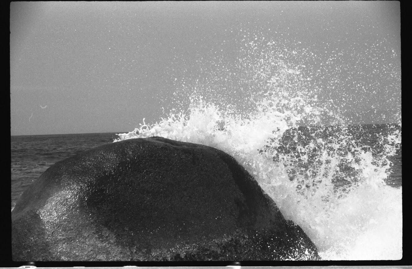 A large rock is being hit by a wave, causing water to splash into the air.