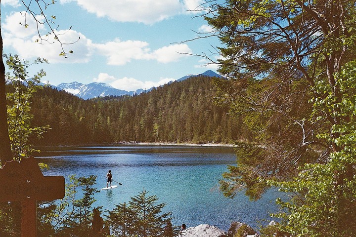 A man paddleboards on a lake surrounded by a forest and mountains.