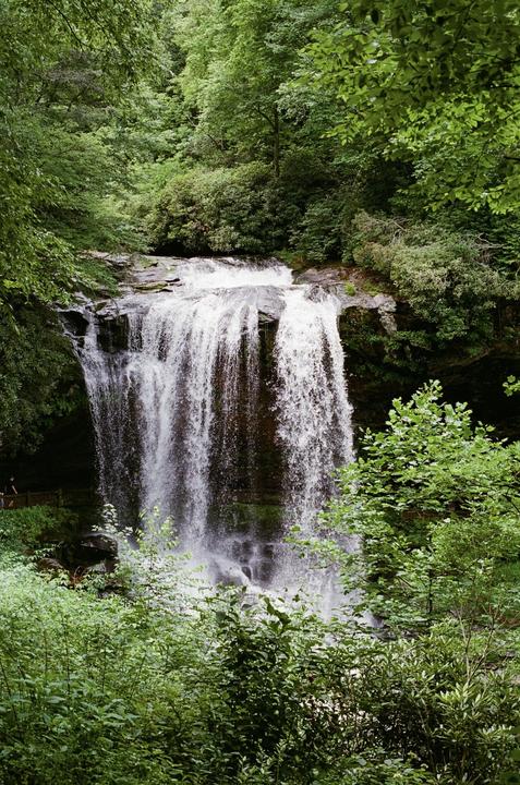 A large waterfall cascades over rocks surrounded by lush green foliage.