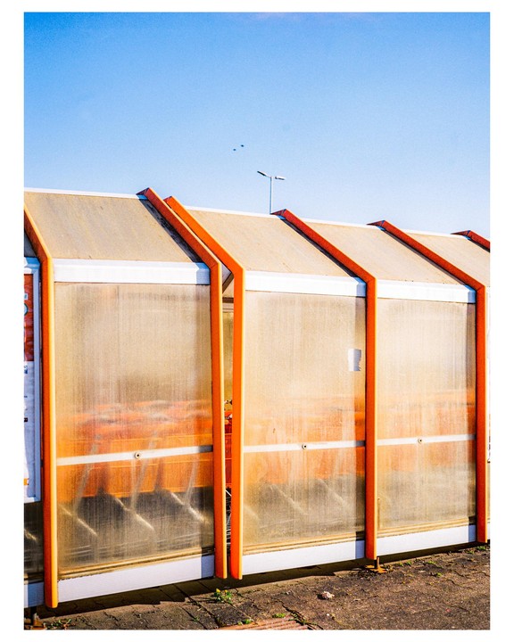 A row of shopping carts are visible through the translucent walls of a cart return shelter under a clear blue sky.