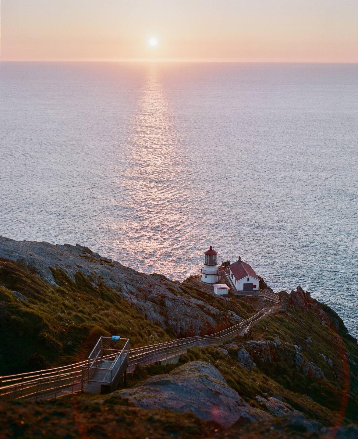 A lighthouse and building sit on a cliff overlooking the ocean at sunset.