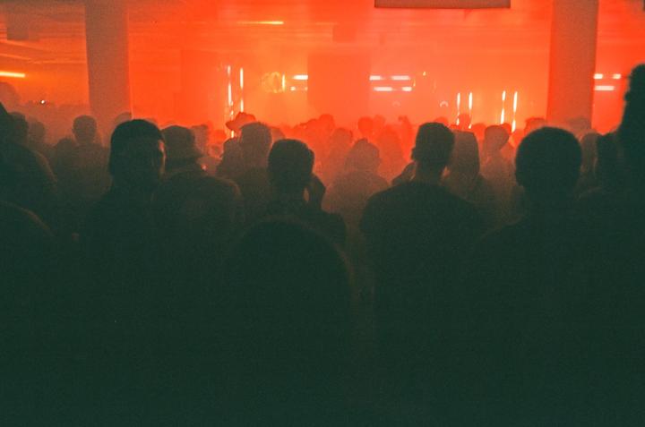 A crowd of people stands in a dark room illuminated by red light.
